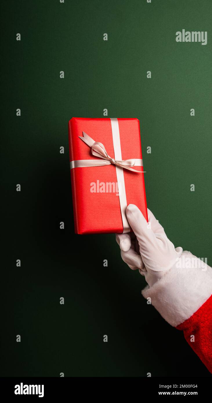 Mano di Babbo Natale corto che tiene i regali contro lo sfondo verde Foto Stock