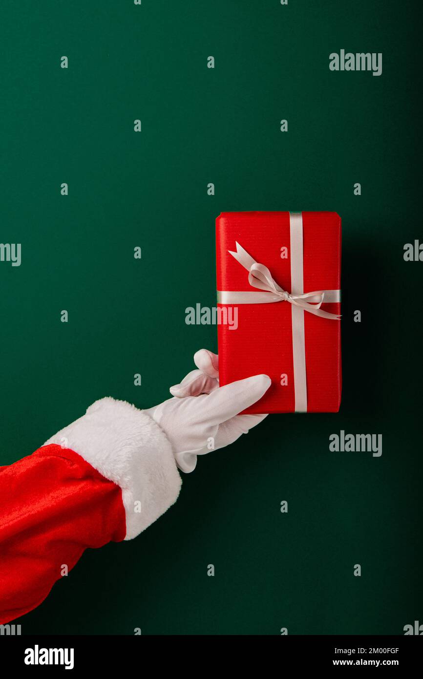 Mano di Babbo Natale corto che tiene i regali contro lo sfondo verde Foto Stock