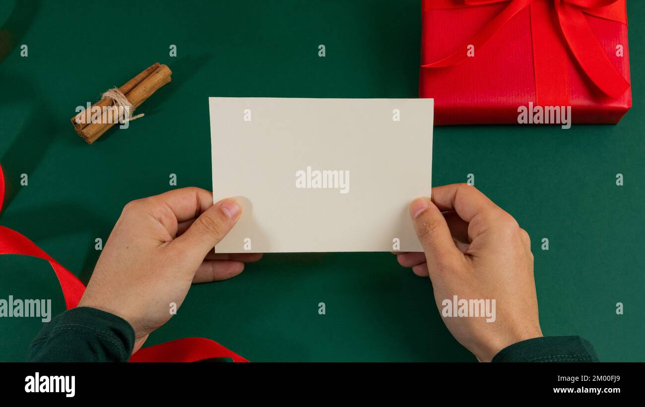 Mani bianche dell'uomo che tengono una cartolina vuota A5 formato sopra un fondo verde con i regali Foto Stock