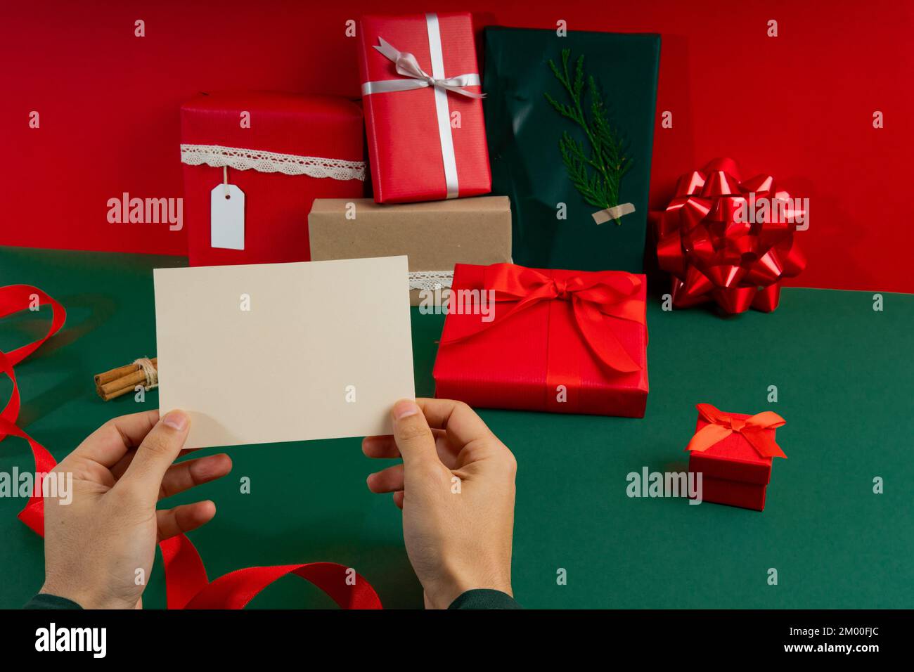 Cartolina mockup con le mani dell'uomo e sfondo verde e rosso con regali Foto Stock