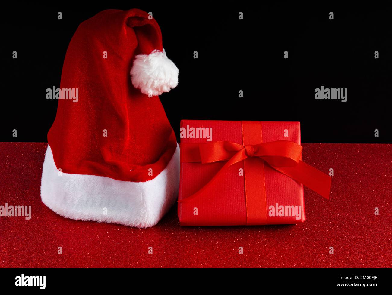 Cappello di Babbo Natale e una scatola regalo rossa sullo sfondo scintillante Foto Stock