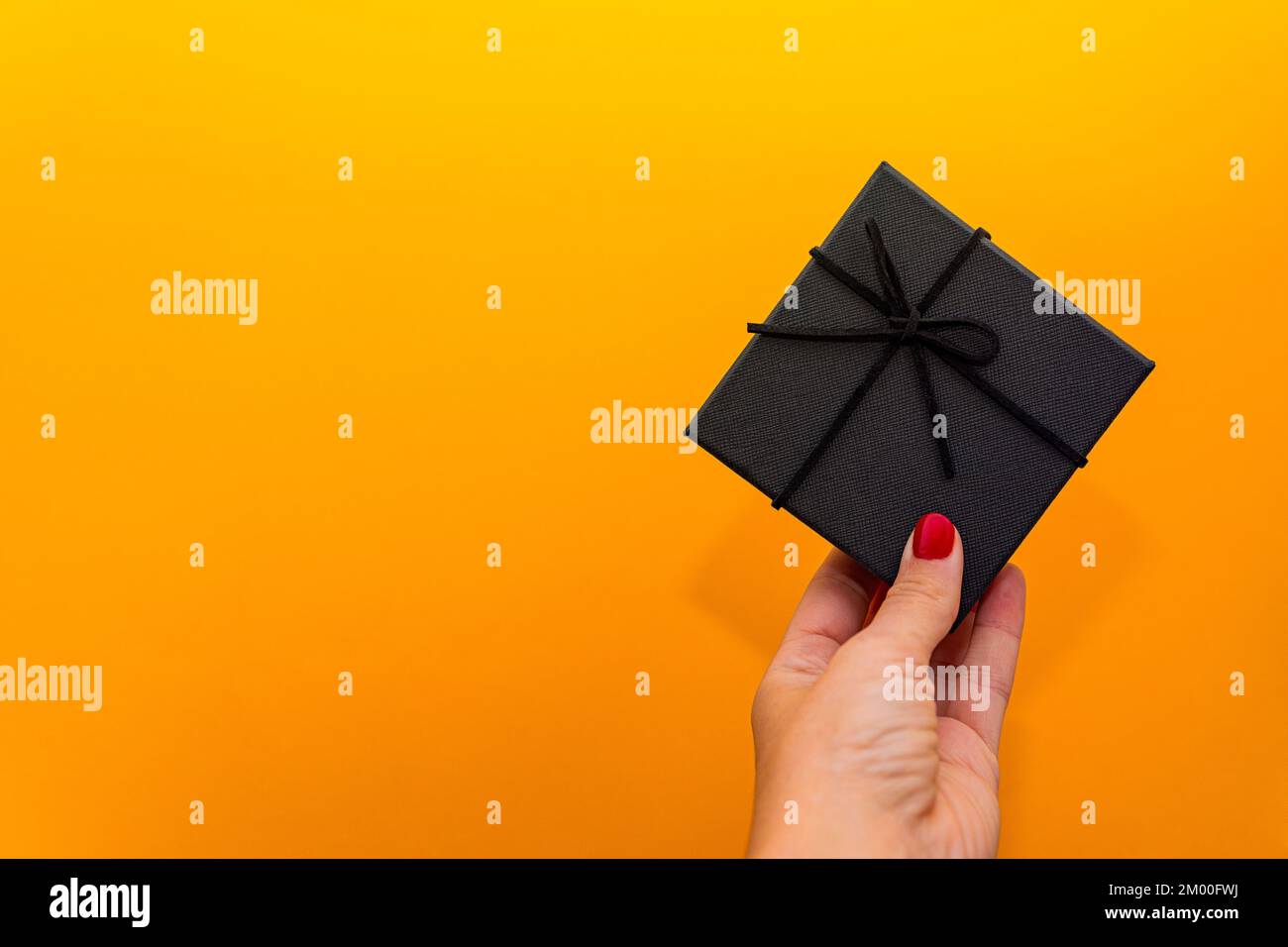 mano della donna con le unghie rosse che tengono il nero presente ove un fondo arancione gradiente Foto Stock