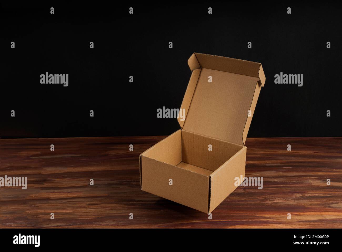 Scatola di cartone marrone aperta sulla superficie di legno con sfondo nero per la simulazione Foto Stock