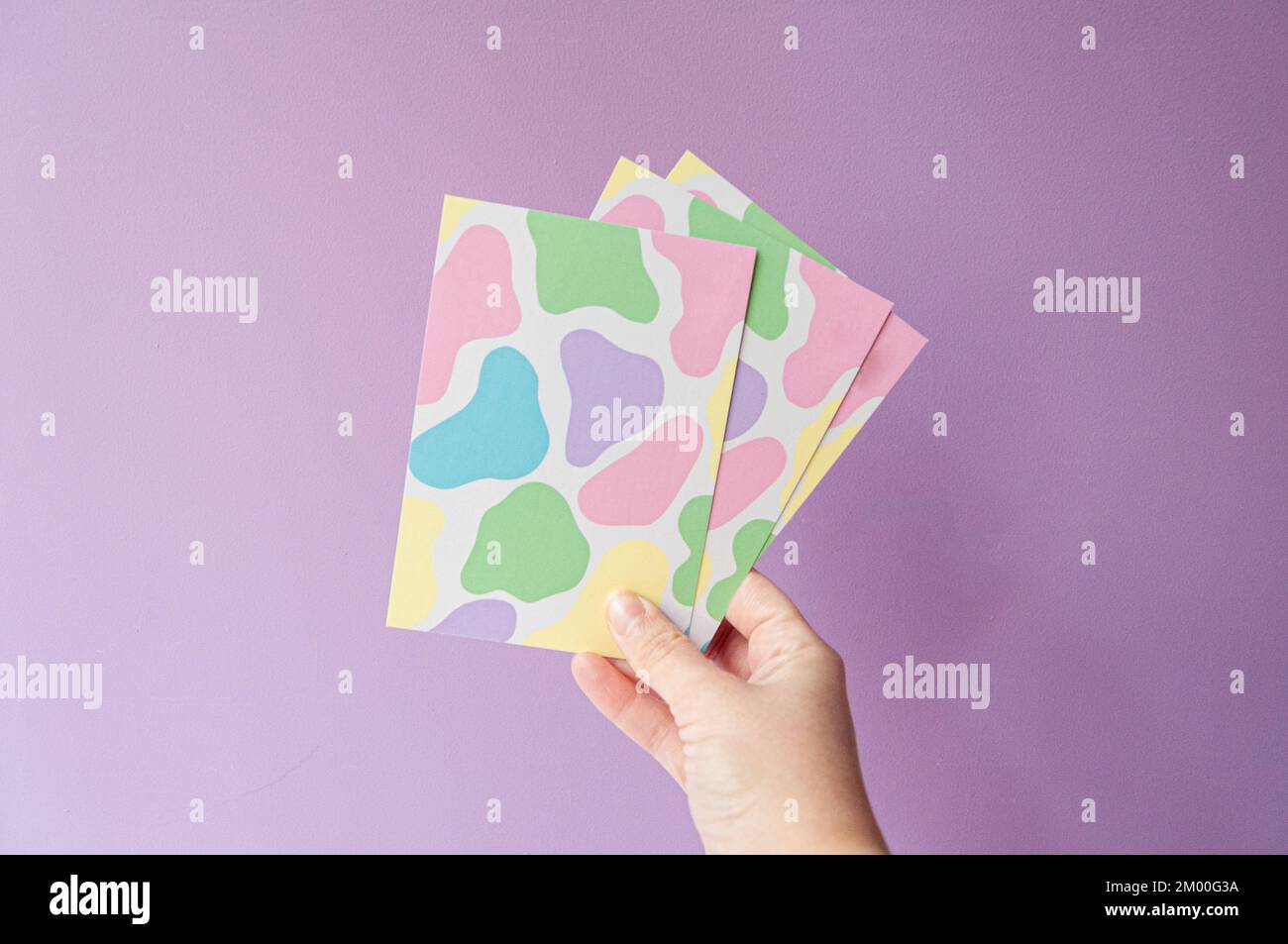 cartoline con un divertente disegno di mucca in colori pastello, tenuto da mano femminile su sfondo lilla. Per e-commerce o piccole imprese Foto Stock