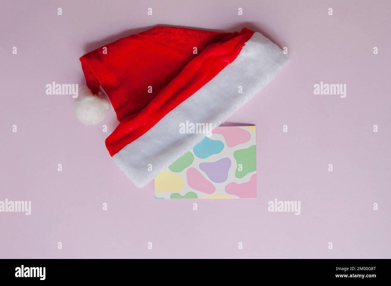 Cappello babbo natale con cartolina con disegno a mucca in colori pastello su sfondo lilla, in formato orizzontale con luce naturale Foto Stock