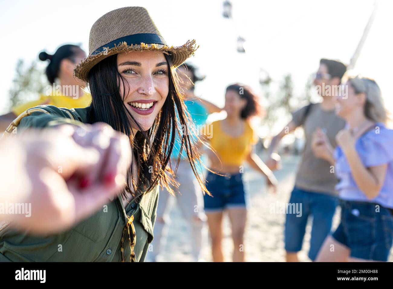 giovane bruna donna con occhi blu che invita a ballare in una festa sulla spiaggia, festival musicale internazionale con una grande folla felice di persone diverse Foto Stock