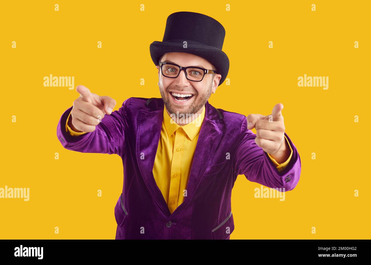 Felice showman non rasato in occhiali sta puntando le dita indice sulla fotocamera su sfondo beige. Foto Stock