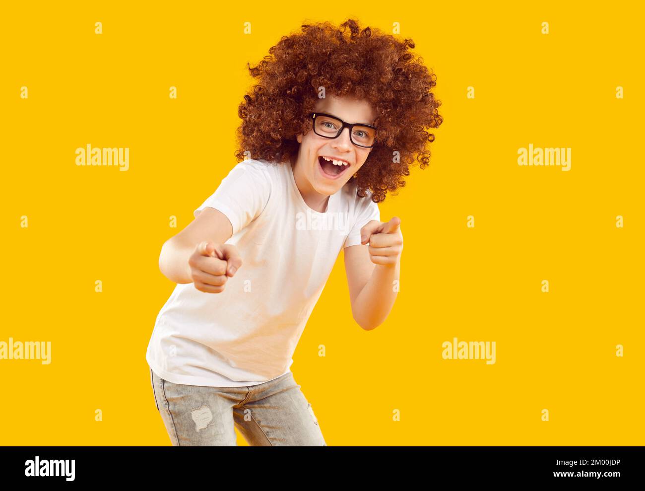 Ragazzo felice vestito in una T-shirt bianca e jeans grigi su sfondo giallo-arancione in studio. Foto Stock
