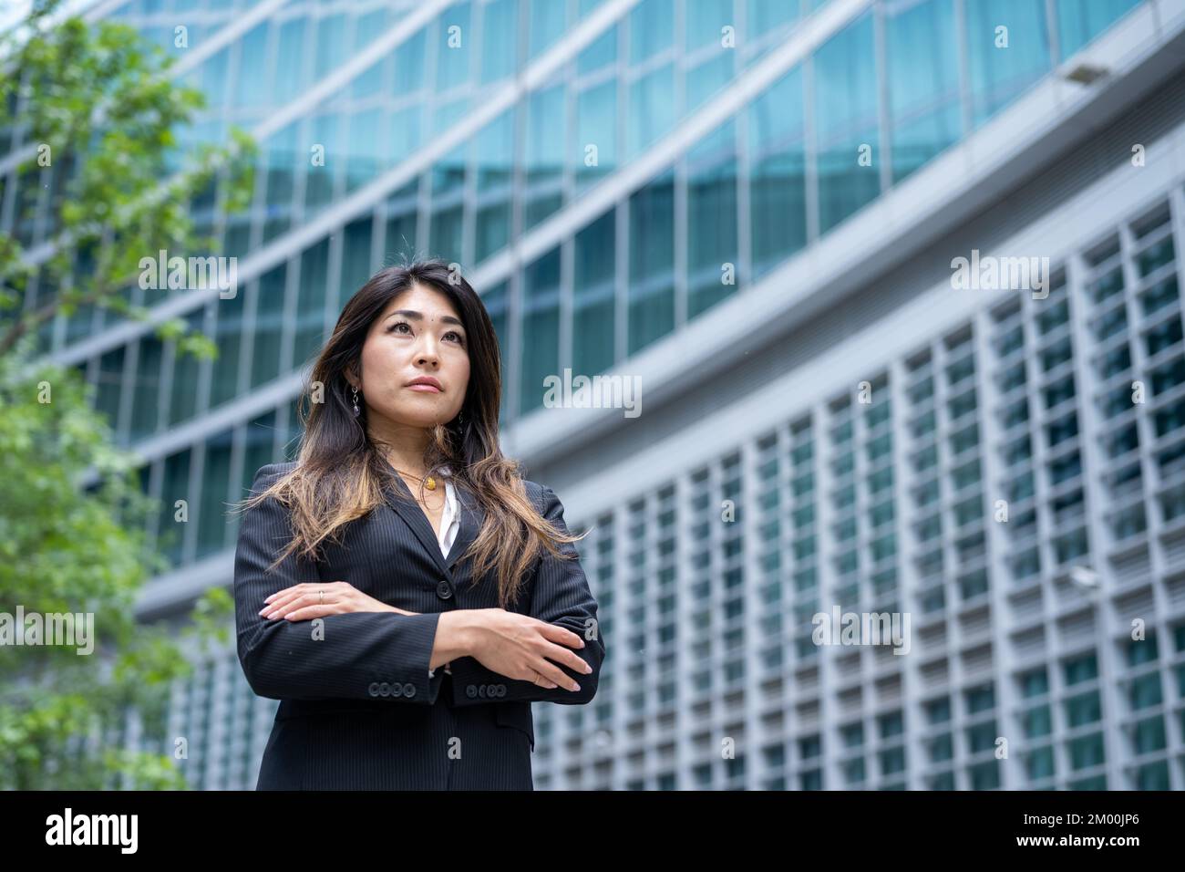 Donna d'affari con braccia incrociate fiducioso per i suoi successi, icona dell'economia verde, donna d'affari di origine giapponese, copia spazio Foto Stock