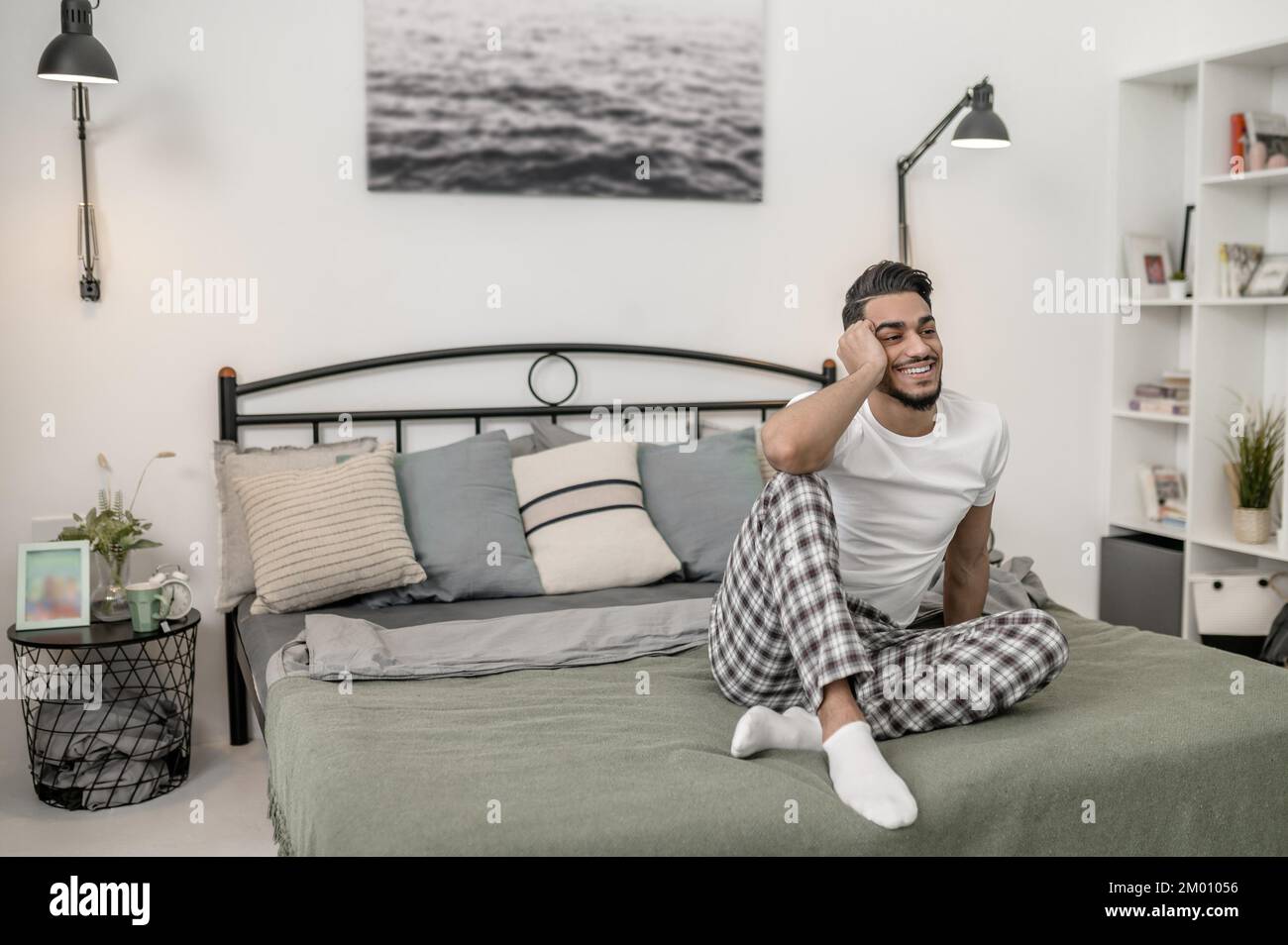 Giorno di chiusura. Un uomo in maglietta bianca e pantaloni a quadri seduti a letto a casa. Foto Stock