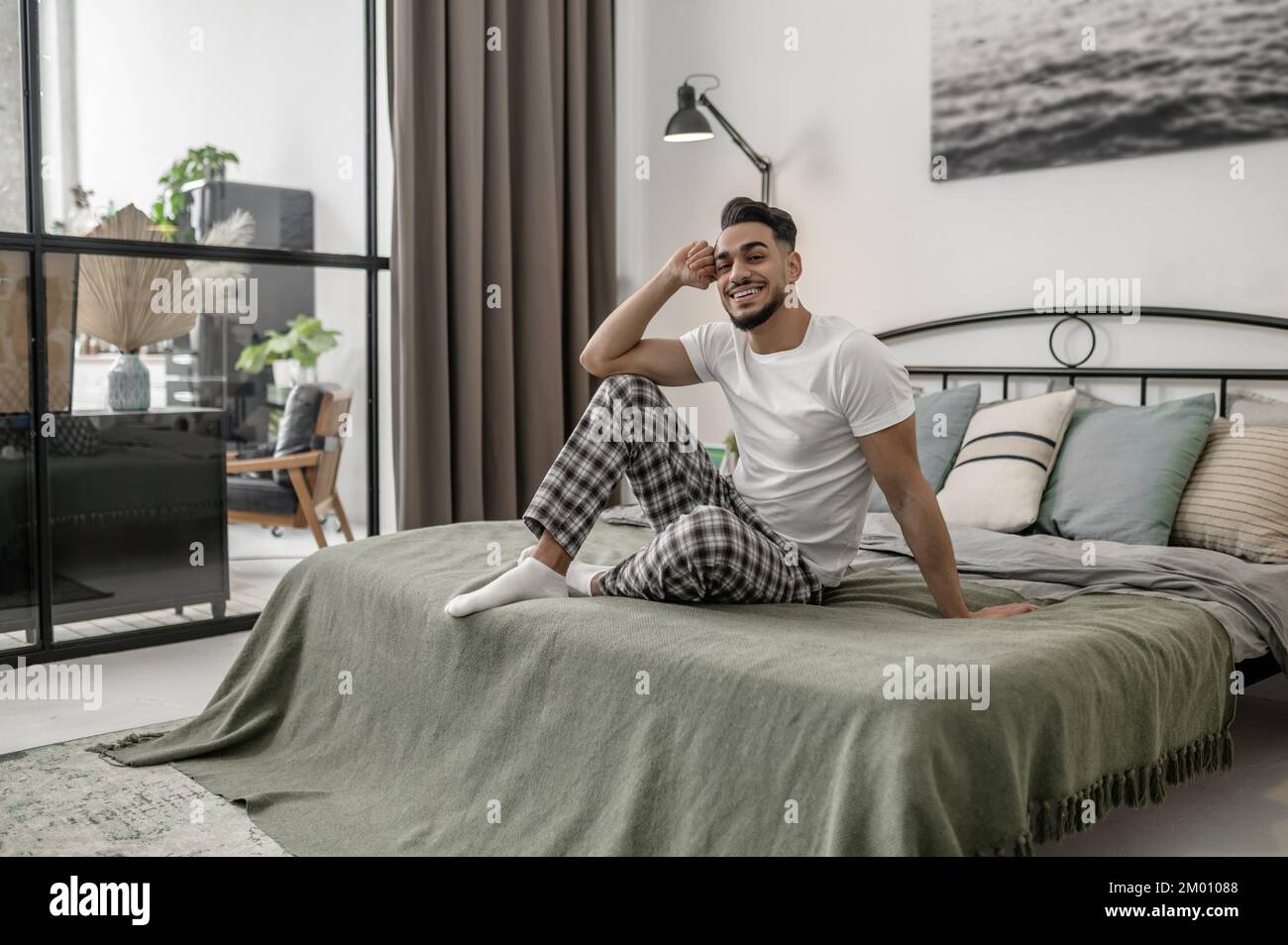 Giorno di chiusura. Un uomo in maglietta bianca e pantaloni a quadri seduti a letto a casa. Foto Stock