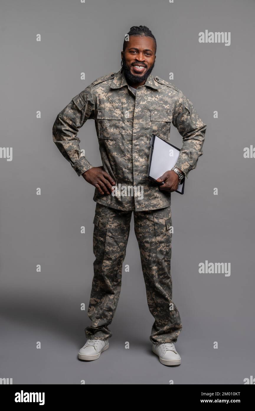 Allegro serviceman in posa per la macchina fotografica contro lo sfondo grigio. Foto Stock