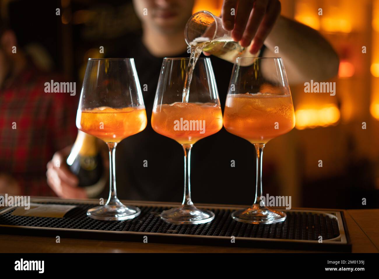 Chiudete tre bicchieri di cocktail al bar. Il barista versa un bicchiere di spumante con Aperol. Spazio di copia Foto Stock