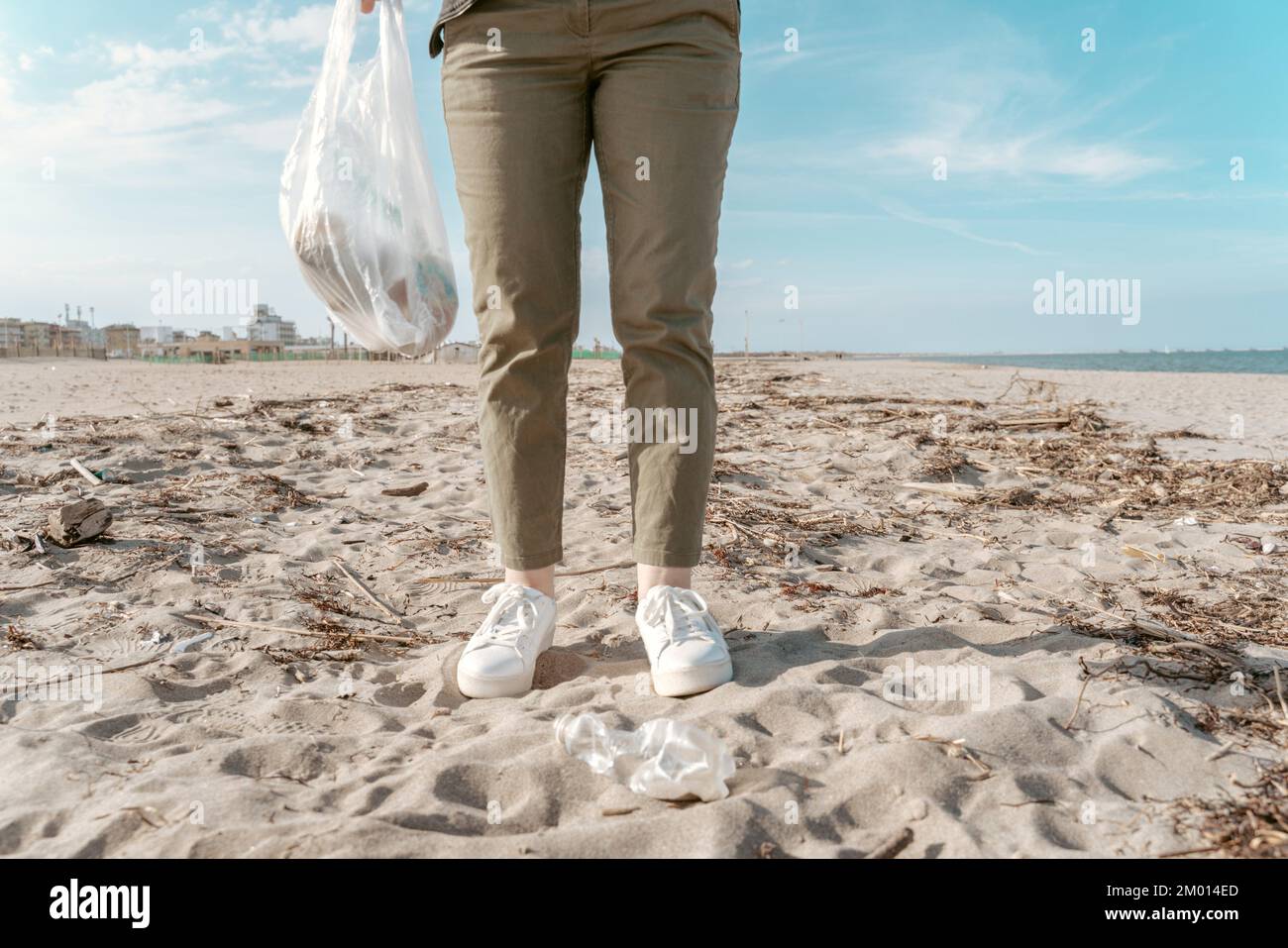 Foto ritagliata di un volontario in piedi sulla spiaggia e tenendo un sacchetto di rifiuti riempito di rifiuti di plastica. Foto Stock
