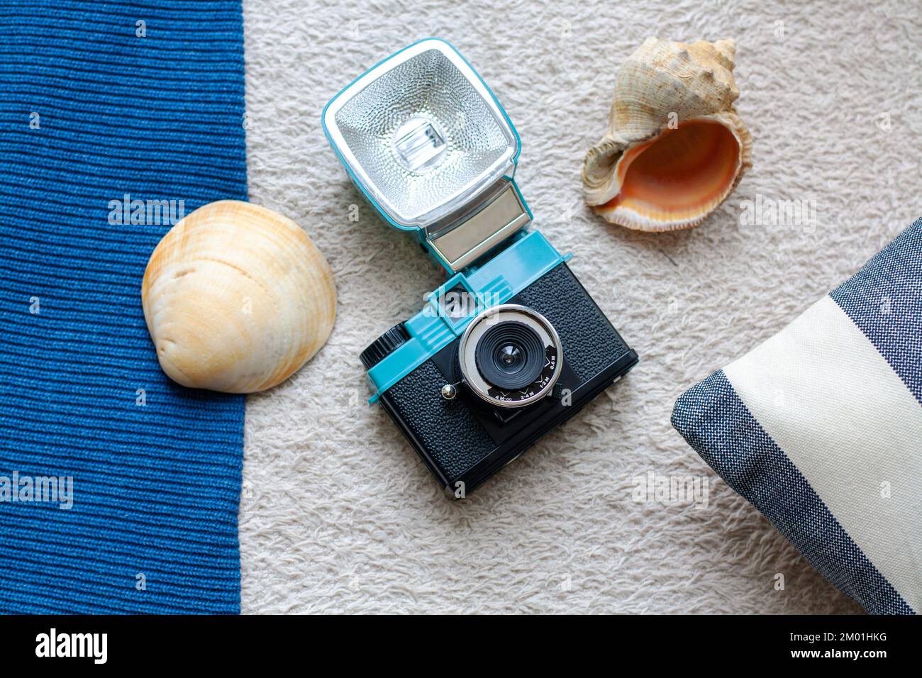Fotocamera a pellicola di plastica, conchiglie marine e cuscino spogliato su uno sfondo in tessuto testurizzato Foto Stock