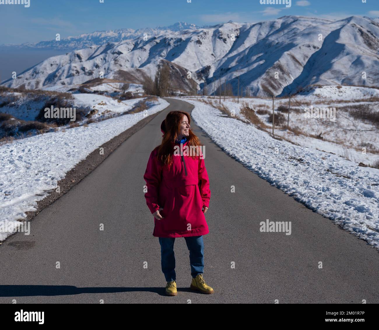 Donna caucasica dai capelli rossi in giacche color fucsia in montagne innevate. Foto Stock