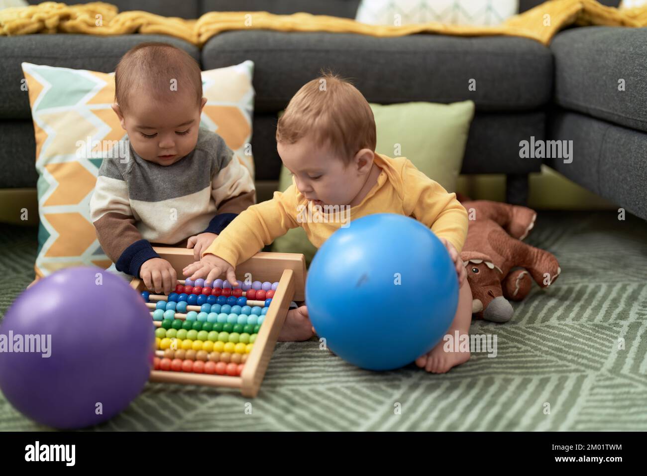 Due bimbi che giocano con palle e abaco seduti sul pavimento a casa Foto  stock - Alamy