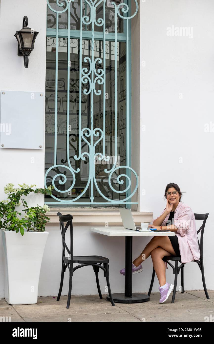 Giovane donna latina con un computer portatile seduto al caffè sul marciapiede - foto d'archivio Foto Stock