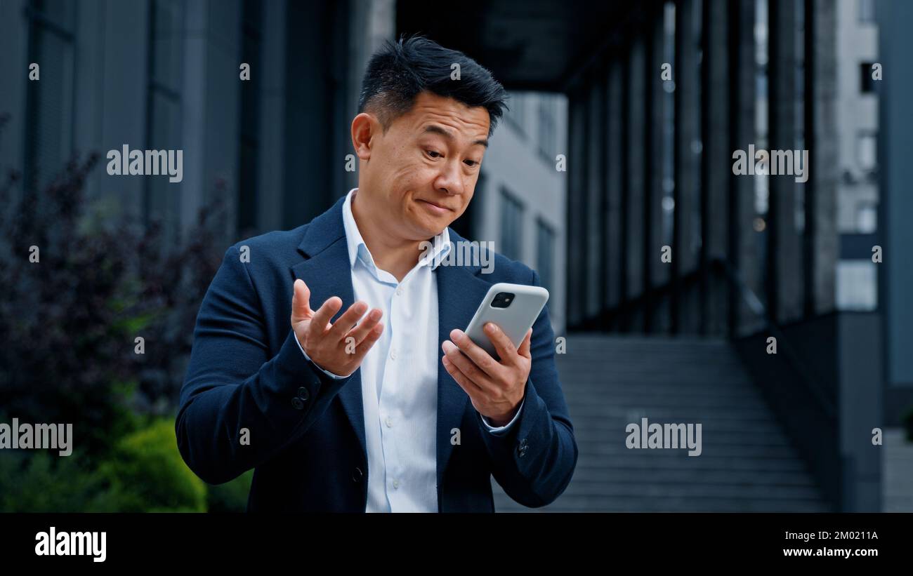 Triste uomo d'affari asiatico in città problema di telefonia mobile. CEO di mezza età imprenditore datore di lavoro outdoor browser telefono sensazione di sconvolto con rotto Foto Stock