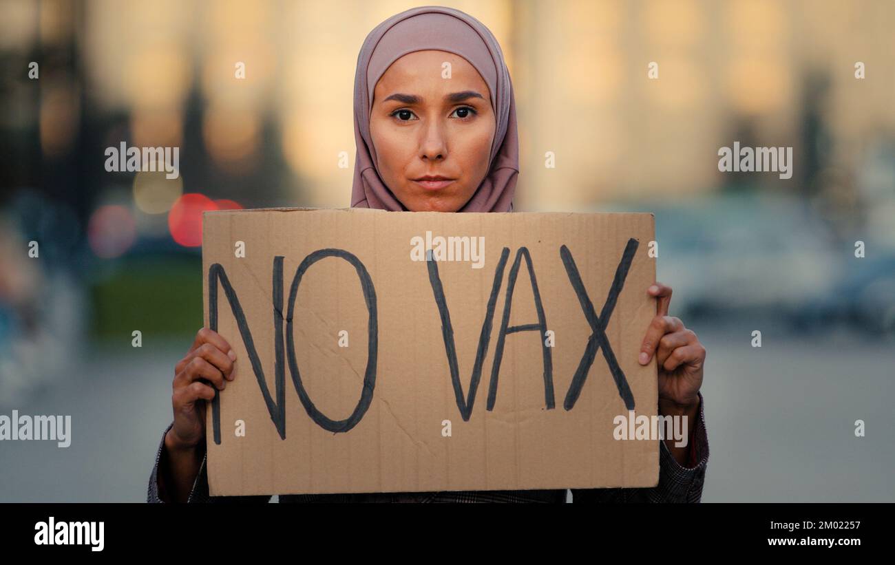 Ritratto femminile musulmana ragazza islamica donna in hijab in piedi in città all'aperto mostrando cartone banner testo non vax protesta contro l'immunizzazione Foto Stock
