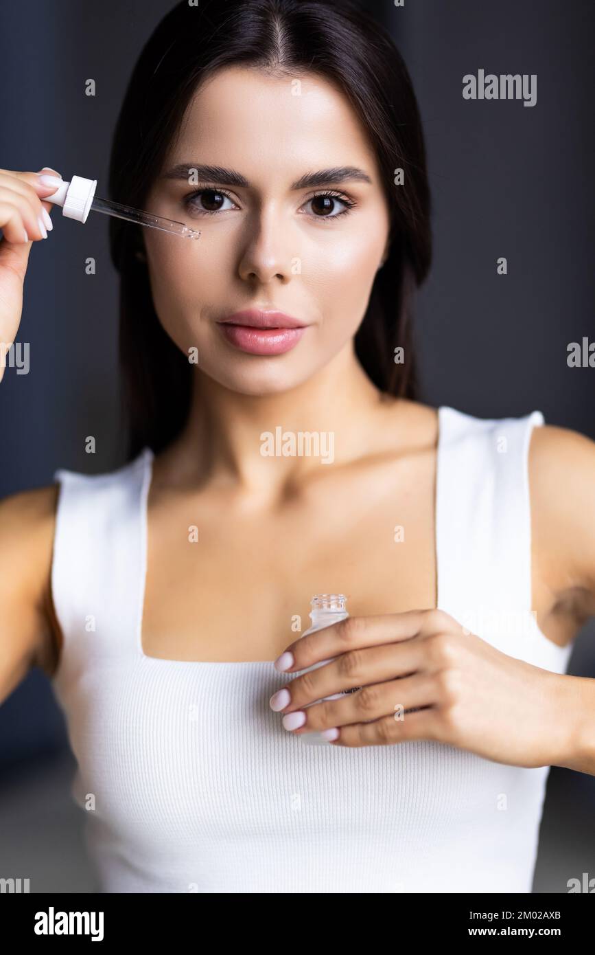 Ragazza allegra che si trova di fronte allo specchio a casa, utilizzando siero per idratare la pelle in estate Foto Stock