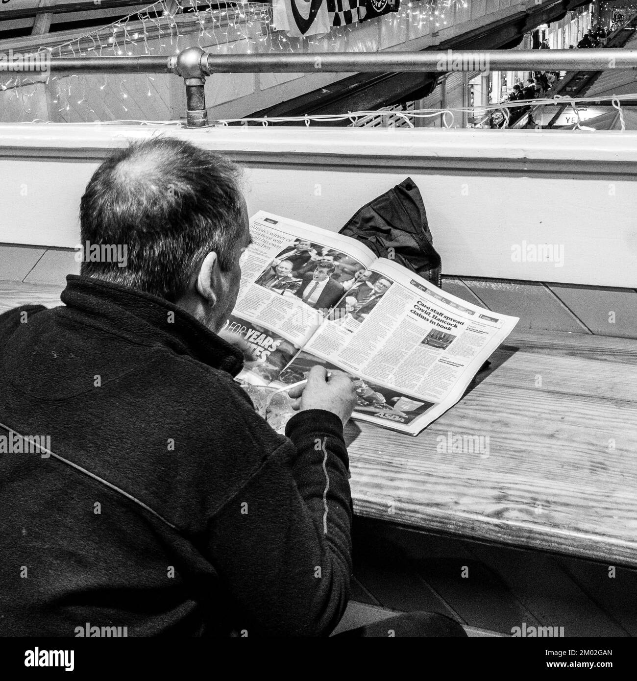 Uomo che legge un giornale mentre mangia una ciotola di zuppa nel mercato interno di Cardiff. Foto chiara dell'articolo su PM Sunak. Fotografia in bianco e nero Foto Stock