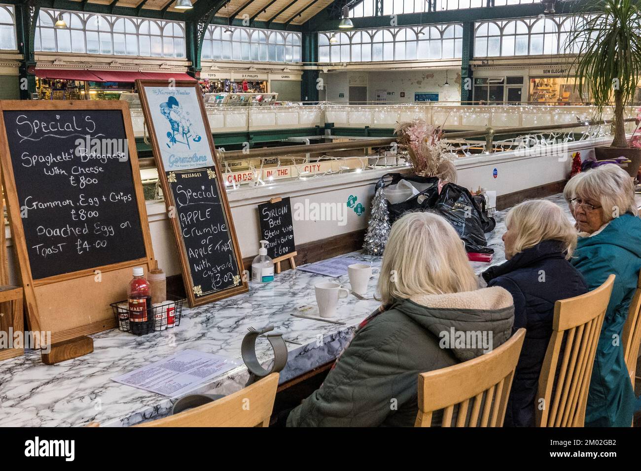 Quattro donne chiacchierano in un bar al livello superiore del mercato interno vittoriano di Cardiff. Tetto in vetro e ripiani in marmo. Menu. Foto Stock