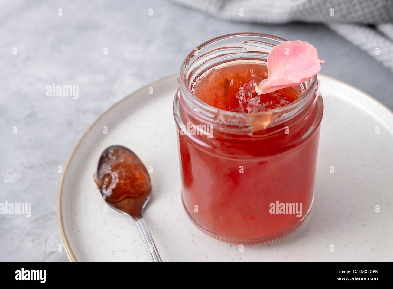 Primo piano di marmellata di rose su fondo neutro con cucchiaio e piatto Foto Stock