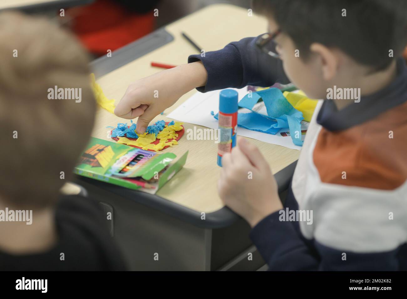 Profondità di campo bassa (fuoco selettivo) dettagli con bambini rifugiati ucraini incollando bandiere ucraine a forma di cuore. Foto Stock