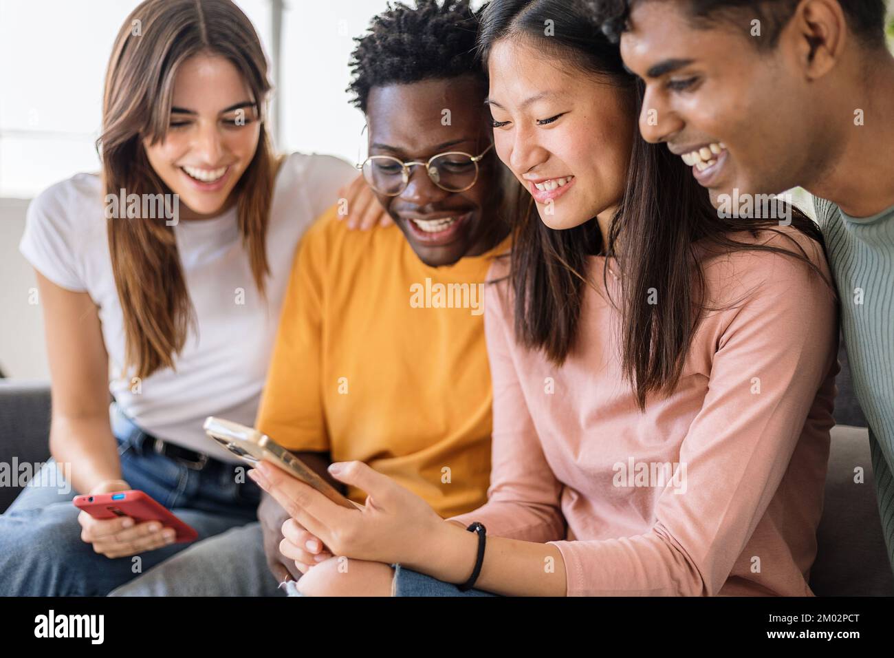 Gruppo di giovani amici adolescenti multietnici che usano il telefono cellulare insieme a casa Foto Stock