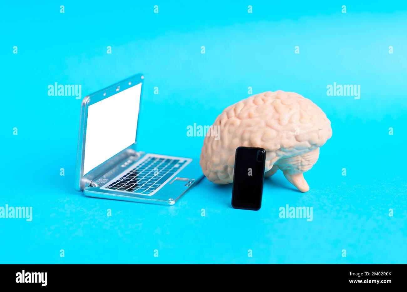 Copia anatomica di un cervello umano posto da mini computer portatile e smartphone figurine isolate su sfondo blu. Creativo saggio commercio in linea delle azione c Foto Stock