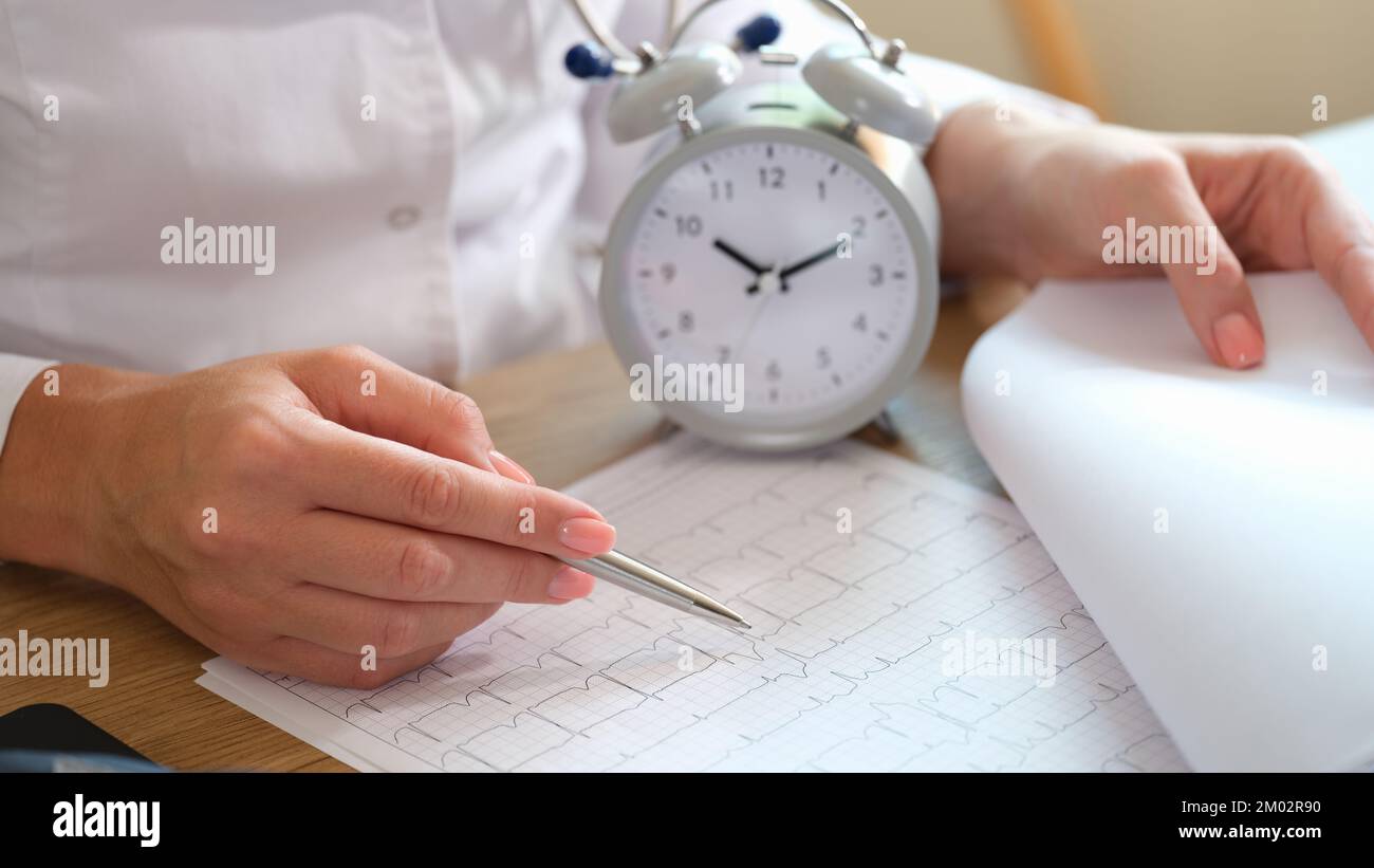 Primo piano della dottoressa con sveglia e cardiogramma sulla scrivania dell'ospedale. Foto Stock