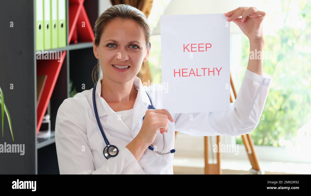 Donna sorridente medico tenendo carta con messaggio mantenere in buona salute. Foto Stock