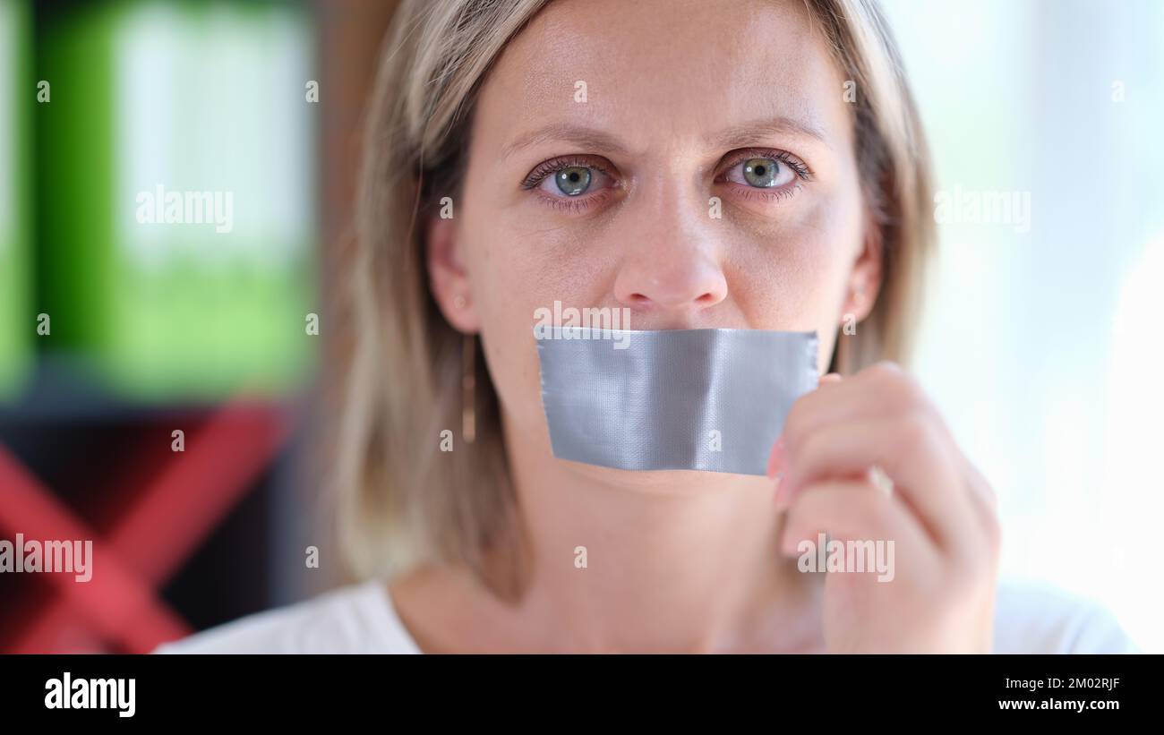 Femmina con faccia seria rimuove il nastro adesivo dal suo vicino della bocca. Foto Stock