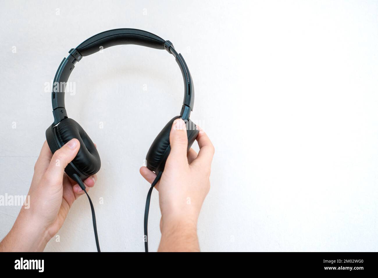Mani che tengono cuffie cablate nere su uno sfondo bianco. Composizione minimalista di apparecchiature audio con spazio per il testo. Foto Stock