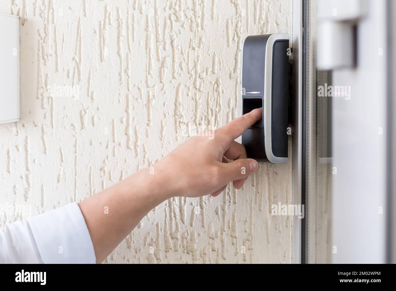 Primo piano. Il dito dell'uomo preme il pulsante del campanello elettronico nero con una fotocamera sulla parete della casa, ufficio. Foto Stock