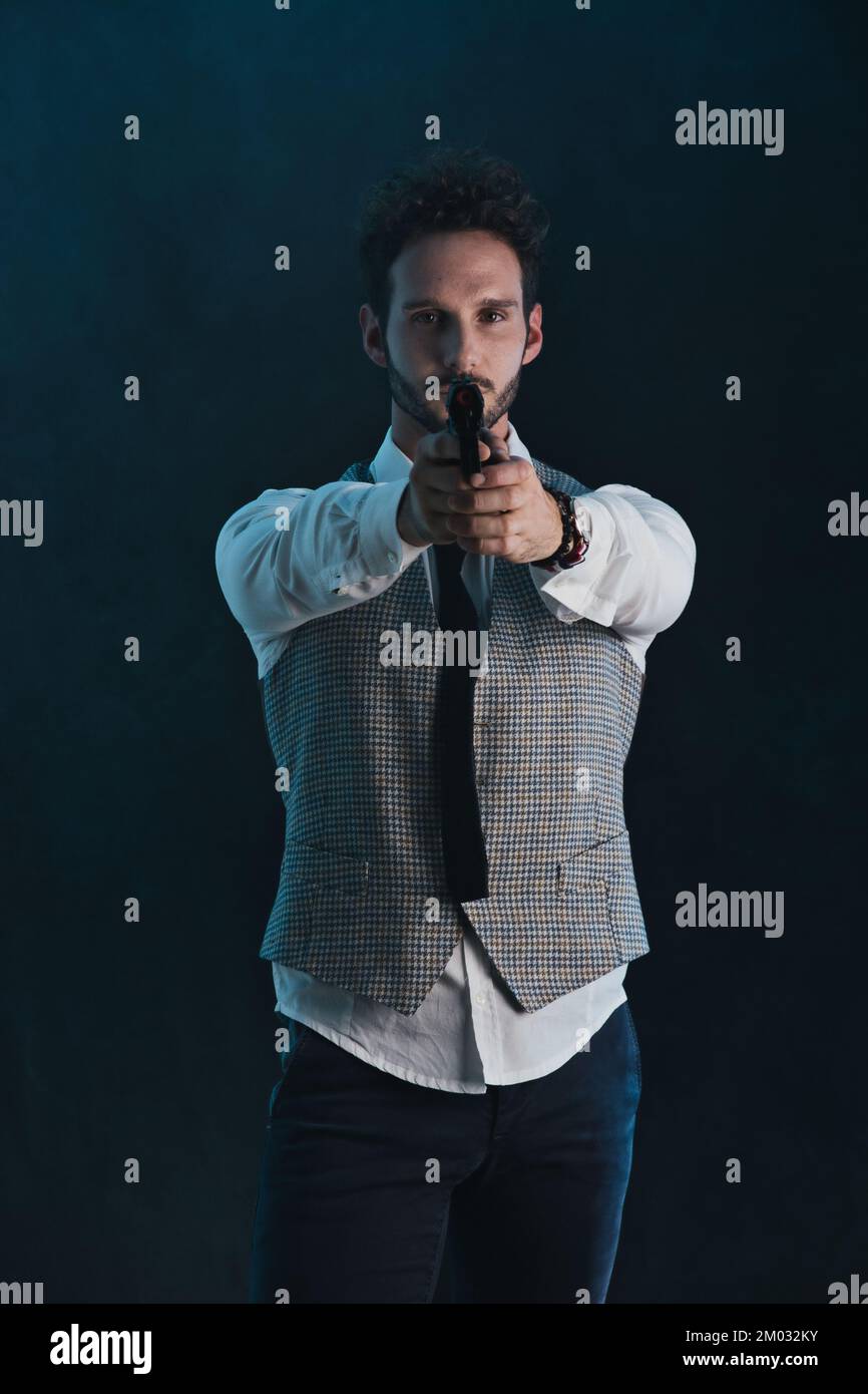 Bell'uomo in studio puntando la pistola, su sfondo scuro Foto Stock