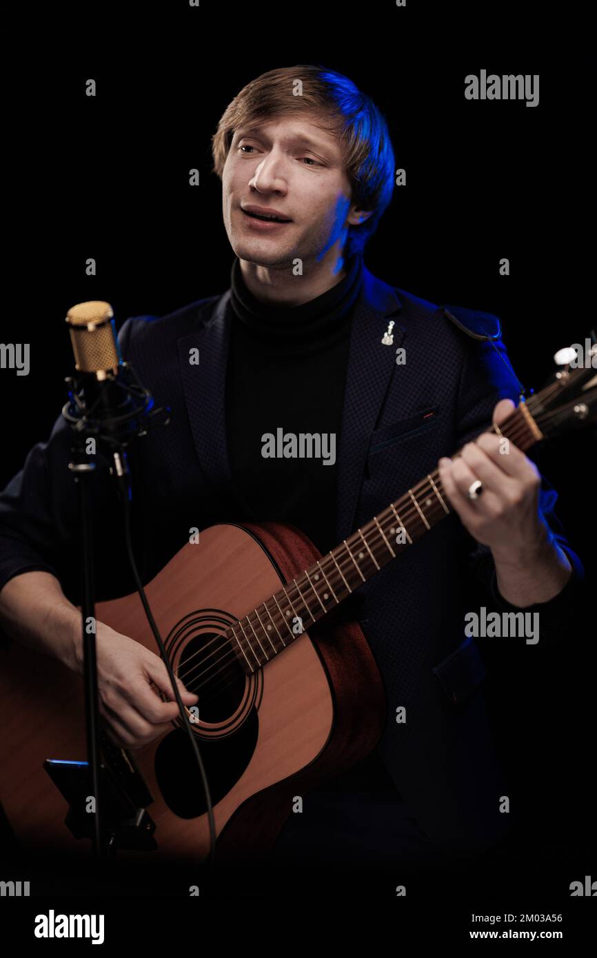 Un musicista maschio con una chitarra in mano che suona, canta e posa su  sfondo nero in una luce panoramica blu Foto stock - Alamy