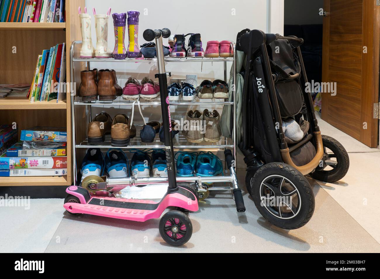 Vivere con i bambini piccoli - scooter per bambini e un passeggino ripiegato appoggiato a un porta scarpe con scarpe per adulti e bambini in una sala. REGNO UNITO Foto Stock