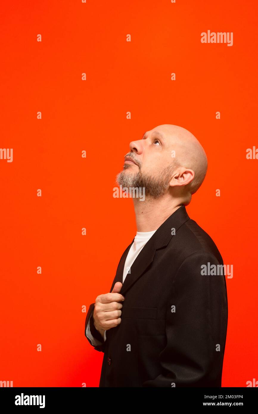 Ritratto di un elegante uomo d'affari che guarda in alto. Isolato su sfondo arancione. Foto Stock