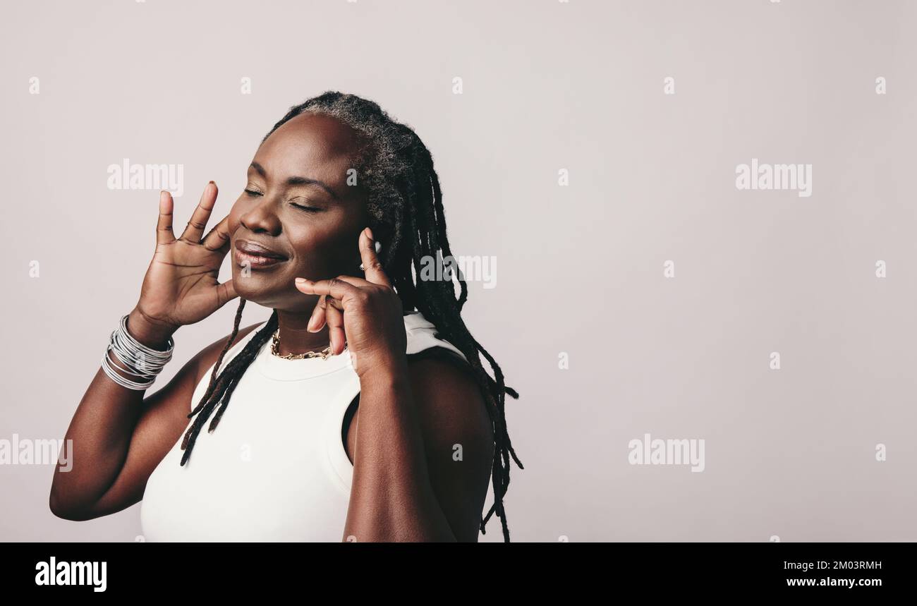 Donna matura con greggi che ascolta la sua musica preferita sugli auricolari bluetooth. Donna di mezza età che ascolta una playlist mentre si trova contro uno stu Foto Stock