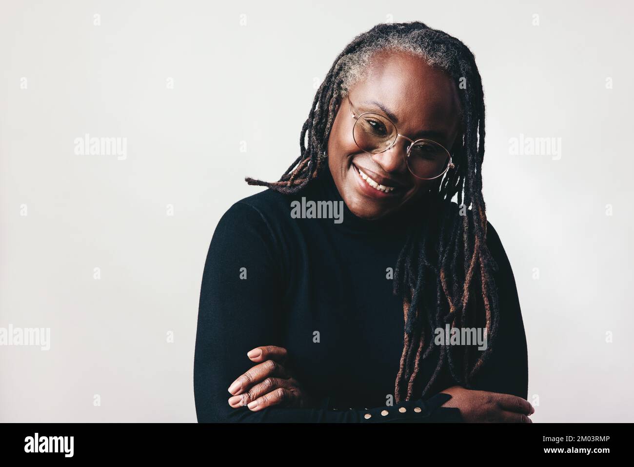 Donna felice professionista sorridente alla macchina fotografica mentre indossa gli occhiali in uno studio. Donna di mezza età con greggi in piedi contro un backgro grigio Foto Stock