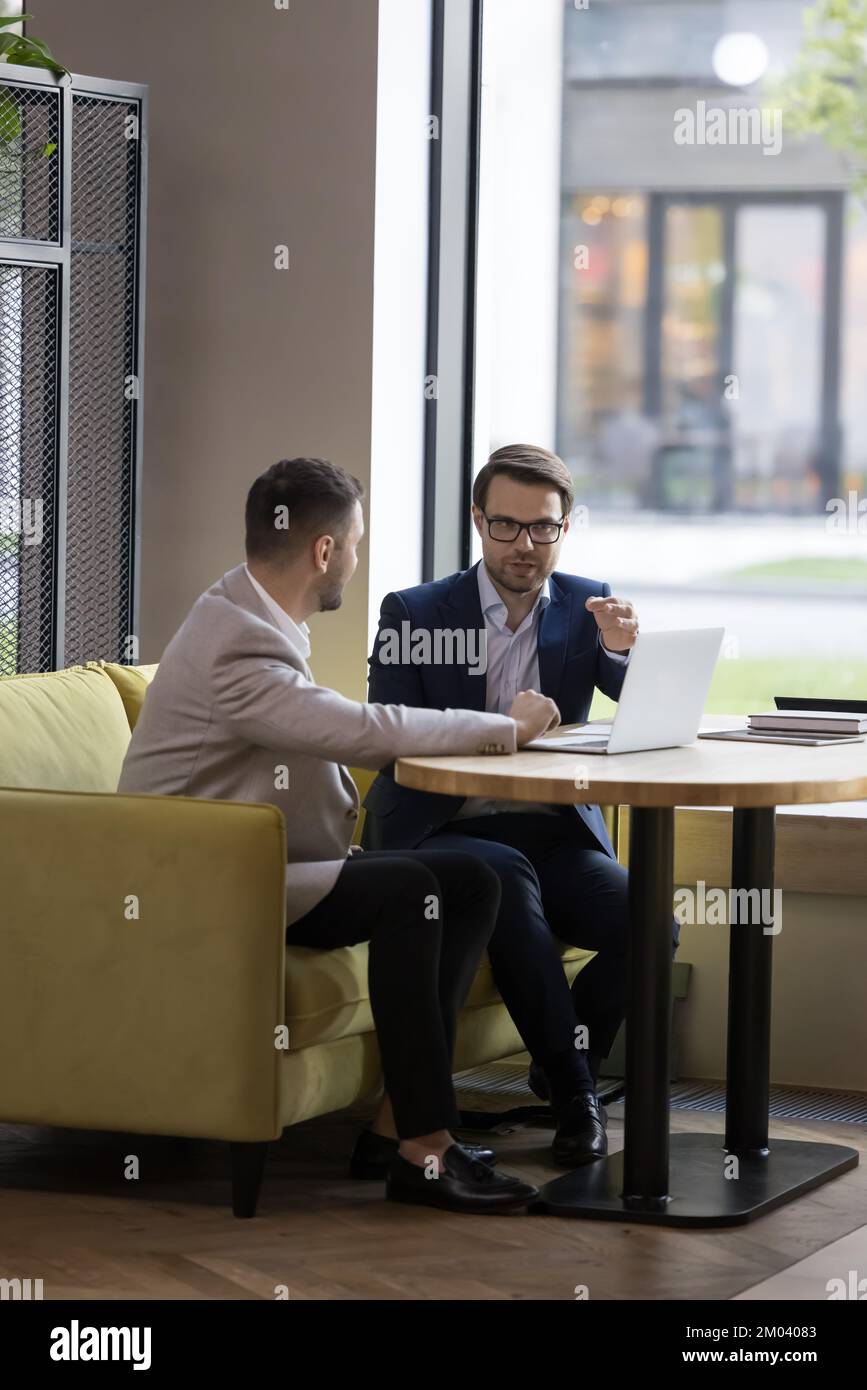 Incontro d'affari in un ufficio moderno di due uomini d'affari con computer portatile Foto Stock