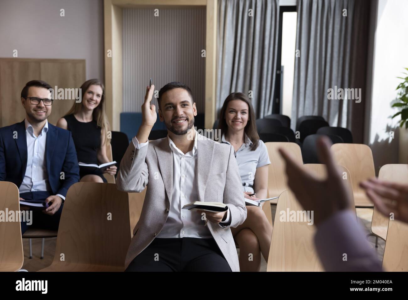 Sorridente partecipante di formazione aziendale che solleva la mano avendo domande al relatore Foto Stock