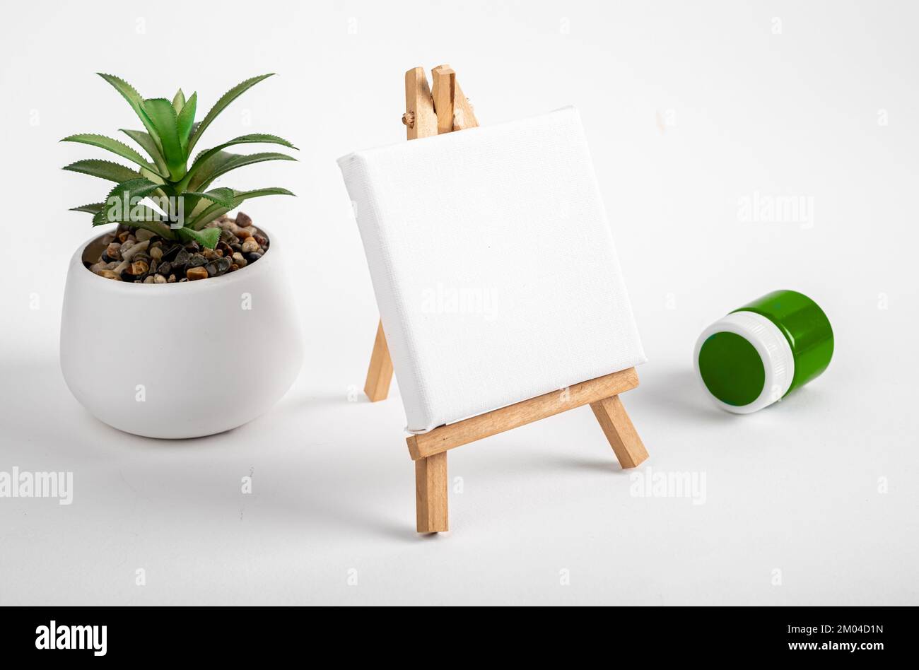 Bianco canvas mockup in prospettiva angolo, mini treppiede in legno, cavalletto e vaso casa pianta, vernice verde in vaso sulla scrivania. Foto di alta qualità Foto Stock