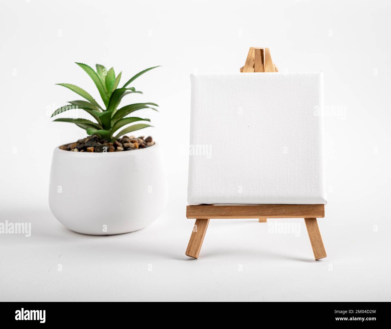 Bianco bianco tela mock up, carta vuota su mini treppiede di legno, cavalletto e vaso casa pianta sulla scrivania. Foto di alta qualità Foto Stock