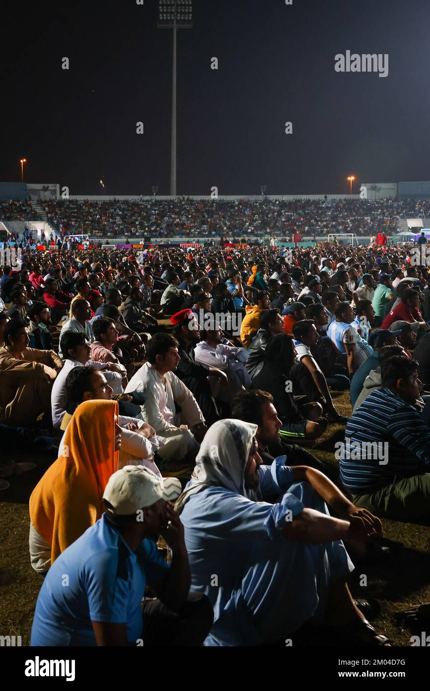 Doha, Qatar. 03rd Dec, 2022. I lavoratori, provenienti principalmente dall'India, dal Bangladesh, dal Nepal e da altri paesi asiatici più poveri, assistono alla partita Argentina-Australia su un grande schermo presso l'Asian Town Cricket Stadium. Nello stadio del cricket, ufficialmente chiamato "Fan zone Industrial Area", migliaia di lavoratori stranieri guardano le partite dei Mondiali ogni sera. Credit: Christian Charisius/dpa/Alamy Live News Foto Stock