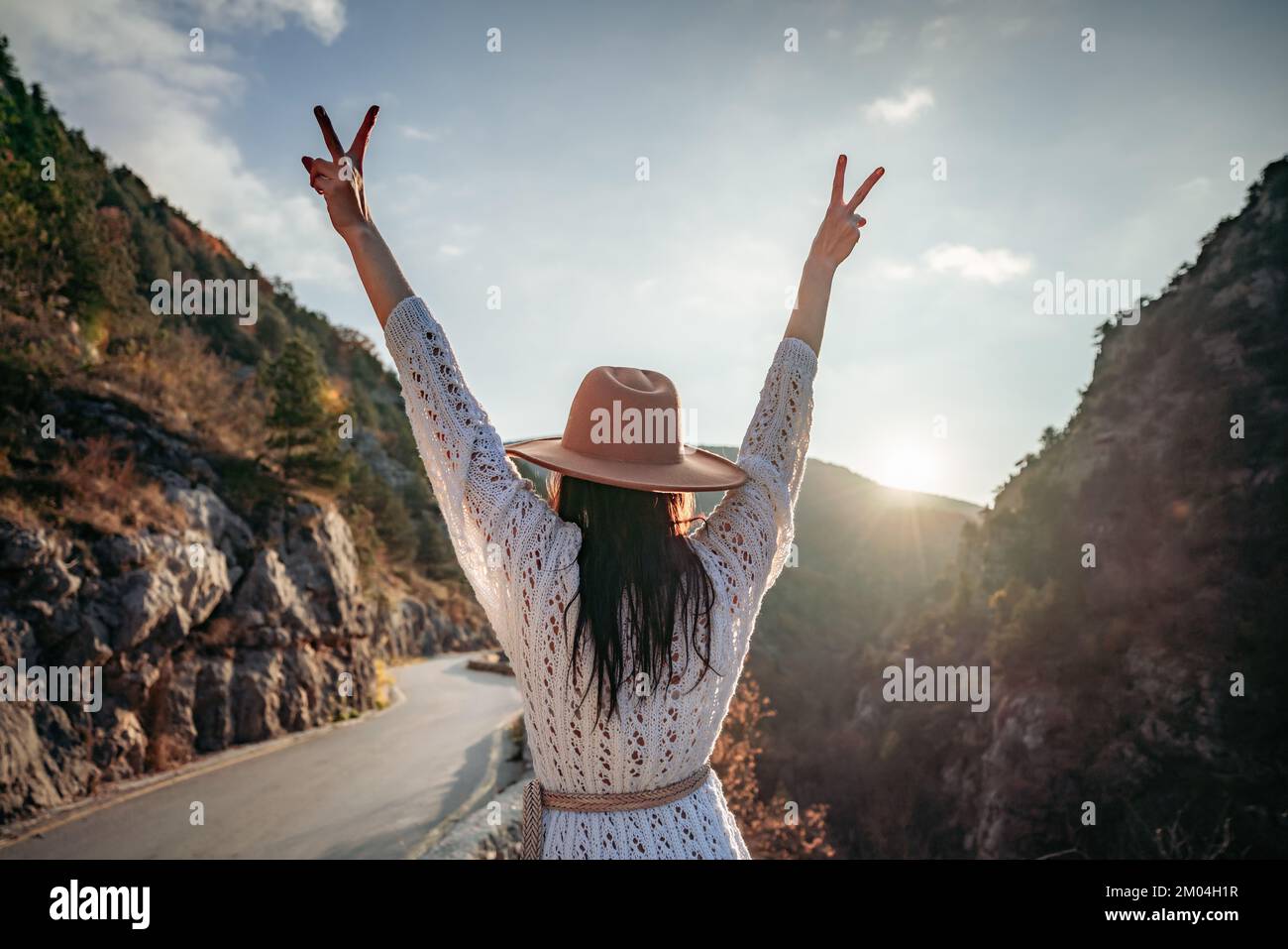 Donna viaggiatore in cappello marrone e maglione bianco che guarda le montagne e la foresta incredibili, il concetto di viaggio wanderlust, momento epico atmosferico Foto Stock