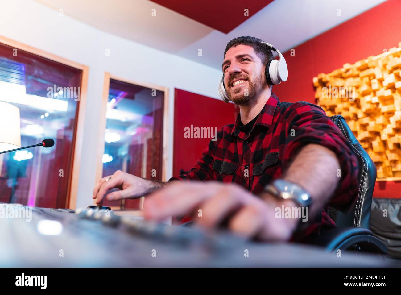 Giovane uomo che equalizza la canzone in uno studio di musica professionale utilizzando il computer indossando cuffie. Buon ingegnere del suono che lavora e mixa la traccia. Concetto di tecnologia. Foto di alta qualità Foto Stock