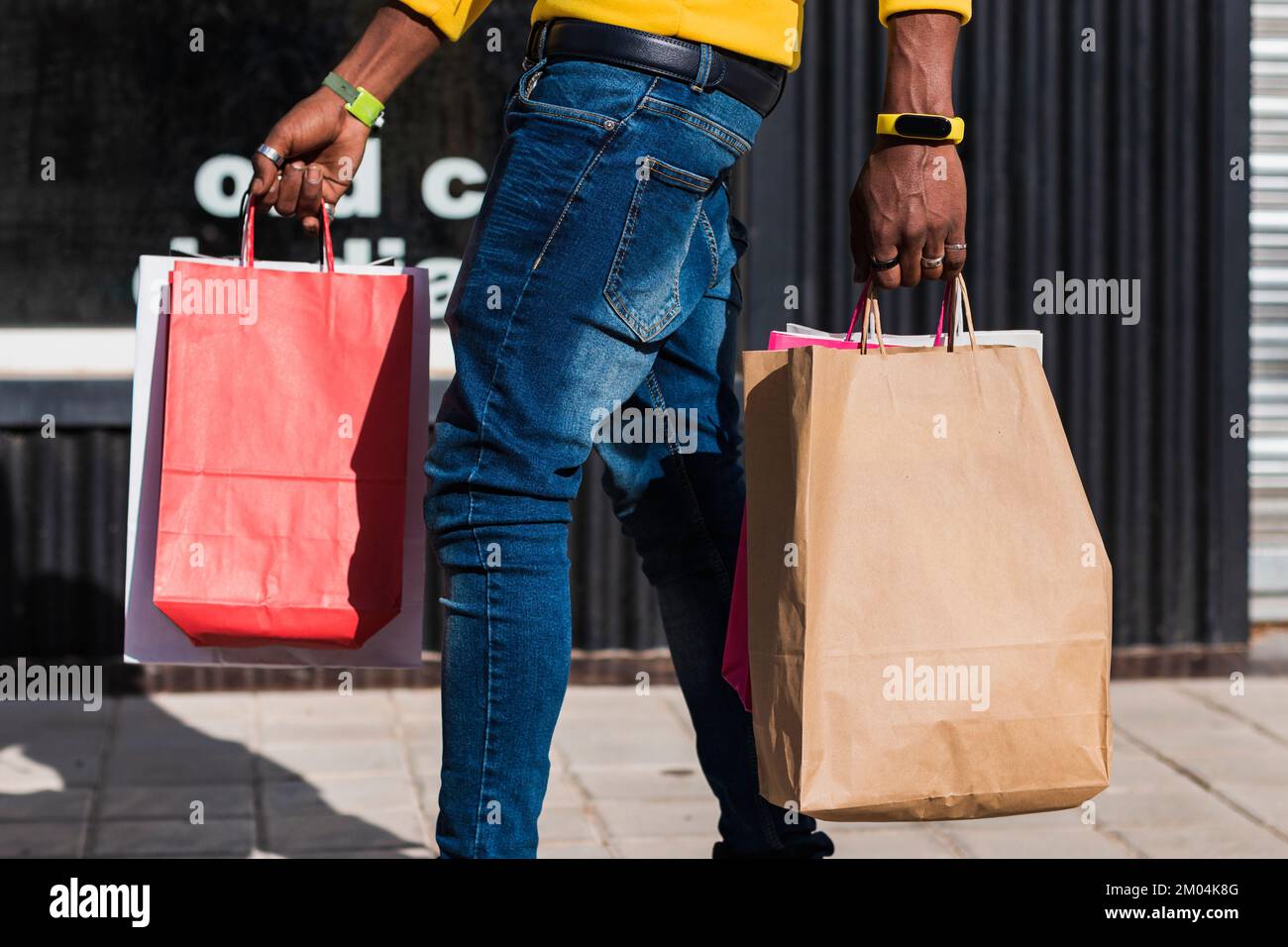 Le mani di un uomo africano sconosciuto vestito di jeans camminando lungo la strada portando diversi sacchetti di carta shopping. Foto Stock
